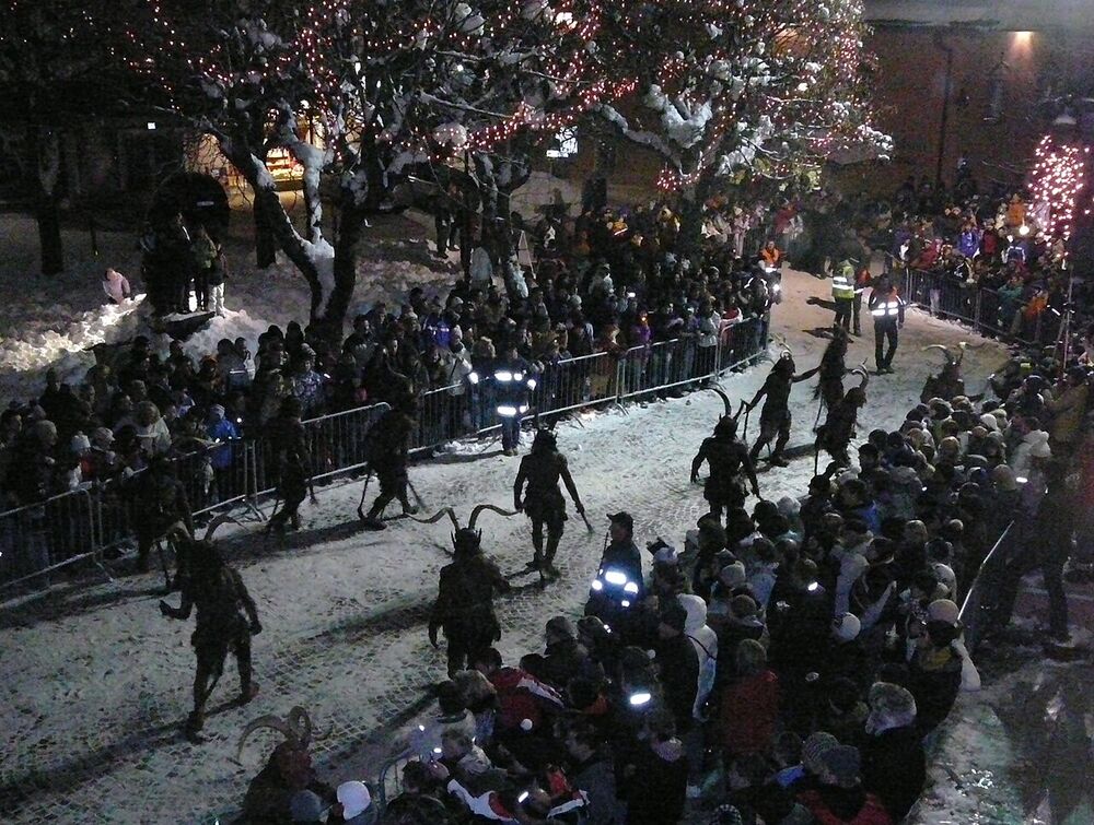 Sfilata notturna di Krampus tra la folla in un paese innevato