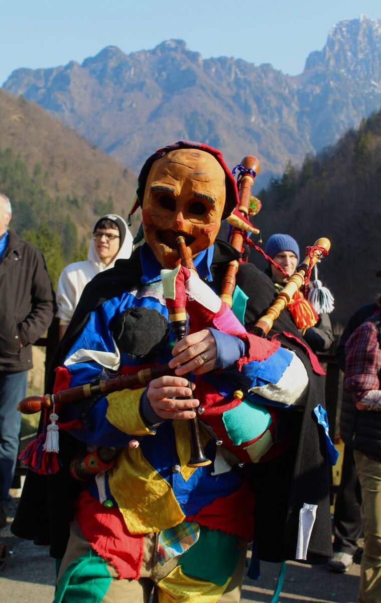 Maschera di legno con vestito a toppe colorate che suona la zampogna